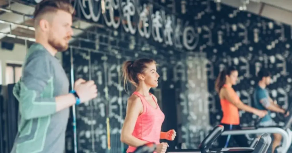 A group of men and women running on treadmills in a modern gym, as part of an HIIT Workout Running Machine session.