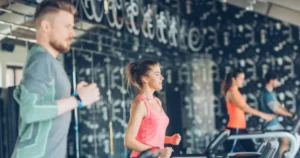 A group of men and women running on treadmills in a modern gym, as part of an HIIT Workout Running Machine session.