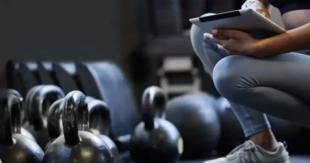 A muscular man performing a diamond push-up inside a gym with an MMA cage in the background.