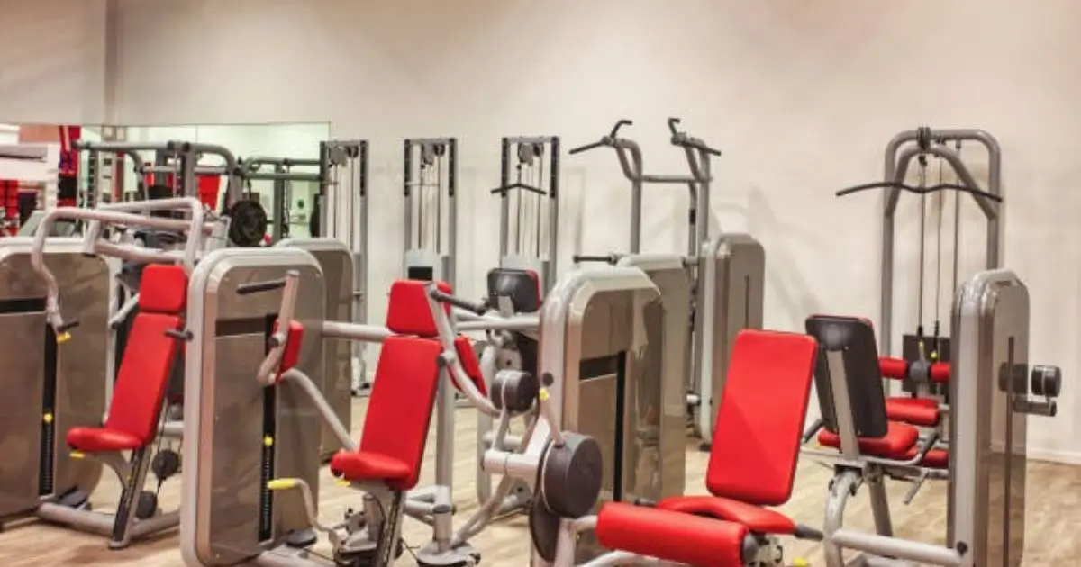 Modern gym with various leg workout machines featuring red seats and metallic frames