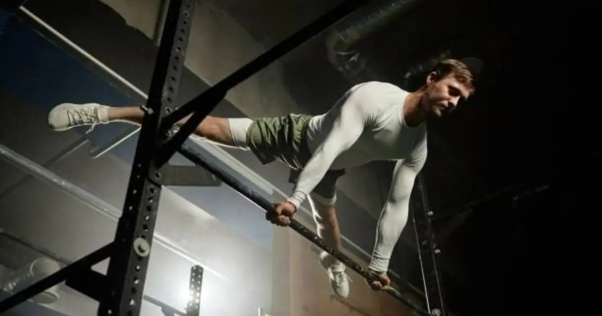 A strong and athletic man performing a full planche calisthenics exercise on a bar in a dimly lit gym, showcasing incredible body control and strength.