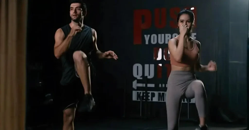Two fit individuals, a man and a woman, engaged in an intense 30 min HIIT workout session in a dimly lit gym, performing high knee exercises. A motivational sign in the background reads "PUSH YOURSELF DON'T QUIT
