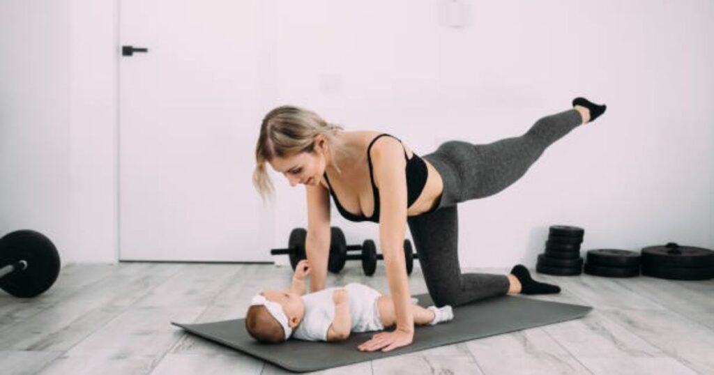 A woman in workout attire is performing a side plank exercise while interacting with her baby, who is lying on a yoga mat. The setting is a clean, minimalist room with dumbbells and weight plates visible in the background.