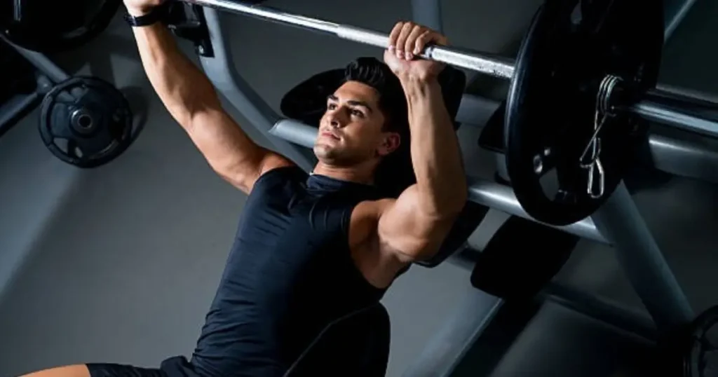 A man in a black shirt is performing a bench press exercise with a barbell, showcasing intense focus and muscle definition.
